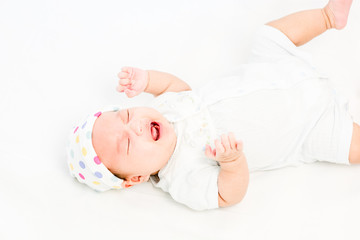 Portrait of a little adorable infant baby girl lying on back on the bed and cry