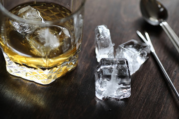 Whiskey in a glass and pieces of ice on a wood