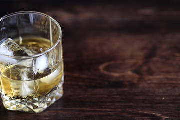 Whiskey in a glass and pieces of ice on a wood