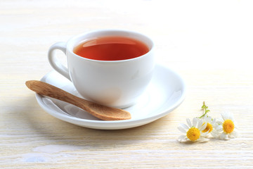 Tea with chamomile and a wooden spoon on a saucer