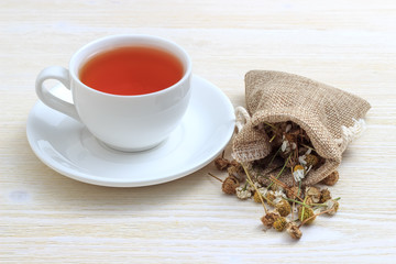 White cup of tea with chamomile in a pouch on a white wooden background