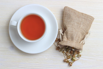 White cup of tea with chamomile in a pouch on a white wooden background