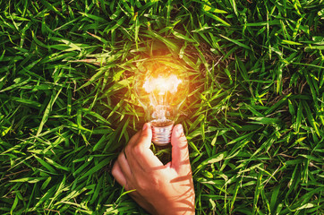 hand hold light bulb on grass  with sunset power energy concept nature