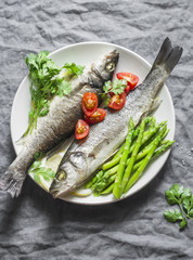 Baked sea bass with asparagus and tomatoes. Healthy diet food concept. On a gray background, top view