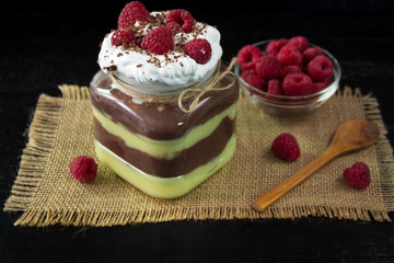Pudinig of vanilla and chocolate sprinkled with whipped cream and raspberries in a glass jar