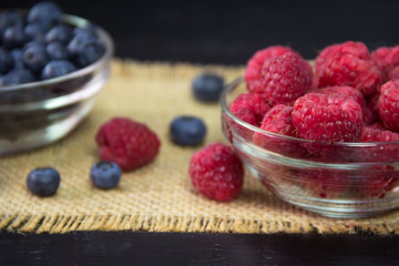 Fresh raspberries and blueberries in bowls on a wooden background. Close-up