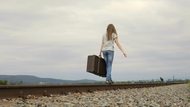Teen girl with suitcase walking on the railway at the day time. Concept of happiness.