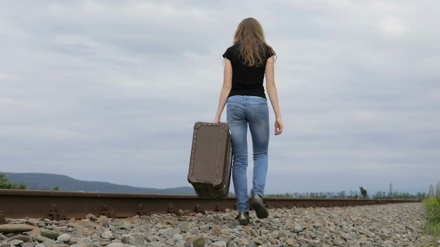 Young sad ten girl walking with suitcase outdoors  on the railway at the day time. Concept of sorrow.