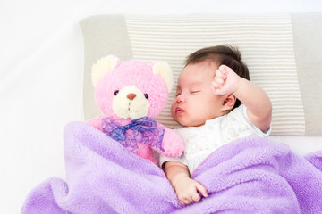 Portrait of sleeping baby  lying on a bed with bear doll