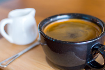 Dark black blue coffee cup with americano coffee, spoon and a milk jug on a wooden stand