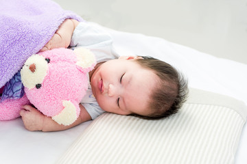 Portrait of sleeping baby  lying on a bed with bear doll