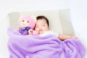 Portrait of sleeping baby  lying on a bed with bear doll