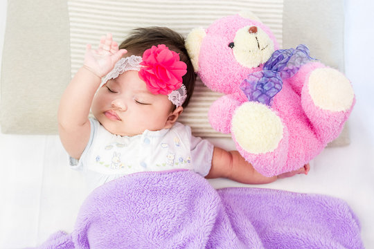 Portrait of sleeping baby  lying on a bed with head band and bear doll