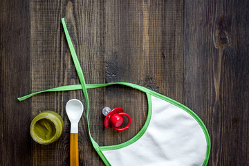 Preparing to feed baby. Puree, spoon, nipple and bib on dark wooden table background top view...