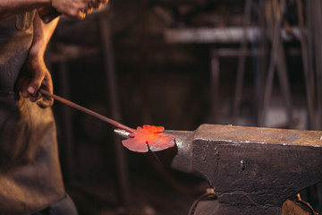 blacksmith manually forging the molten metal on the anvil in smithy with spark fireworks