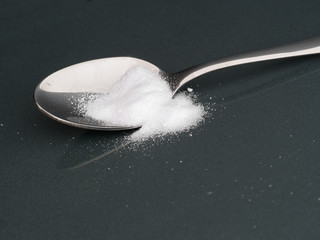 Spoon with artificial sweetener. On shiny grey.
