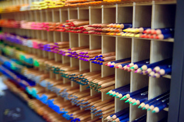 Multicolored pencils in art store in wooden cells closeup, selective focus. Artspace, workshop, creativity concept. Modern art.