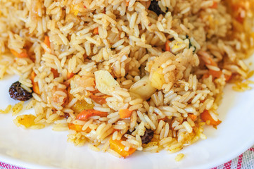 Pilaf with vegetables, raisins and herbs on a white plate. Healthy vegetarian food. Selective focus.