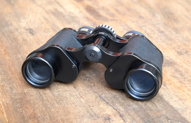 Old prism black color binoculars on vintage wooden background front view closeup