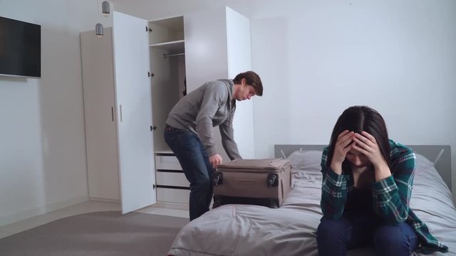 Funny divorce in young family. Caucasian boyfriend or husband packing clothes in suitcase and leave apartment. Young woman happy smiling and celebrating separation.