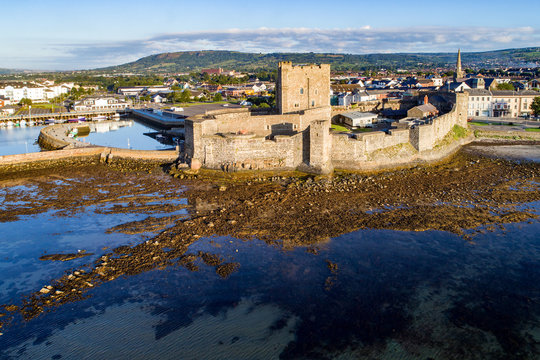 Medieval Norman Castle in Carrickfergus near Belfast in sunrise light. Aerial view with marina, yachts, parking and town in the background.