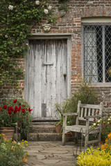 Fototapeta na wymiar Quintessential old English country garden image of wooden chair next to vintage back door