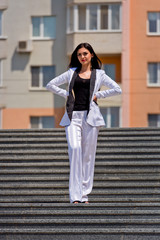 Charming young brunette posing in front of the camera on the steps in the city.