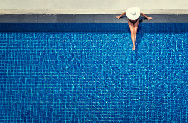 Enjoying suntan. Vacation concept. Top view of slim young woman in hat in the big swimming pool.