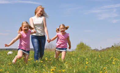 A young mother takes her twin daughters out for a walk  in a flower field. The children enjoy  running and jumping through the