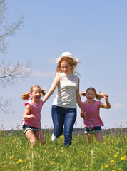 A young mother takes her twin daughters out for a walk  in a flower field. The children enjoy  running and jumping through the