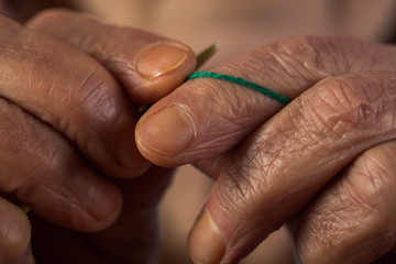 Knitting old hands and fingers holding knitting needle and woolen thread, grandmother prepares scarf or sweater, hands with wrinkles, retired hobbies in retirement, memories of grandmother, vintage 