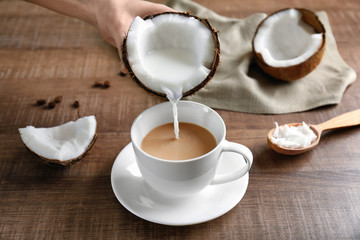Woman pouring coconut milk from nut into cup of coffee on table