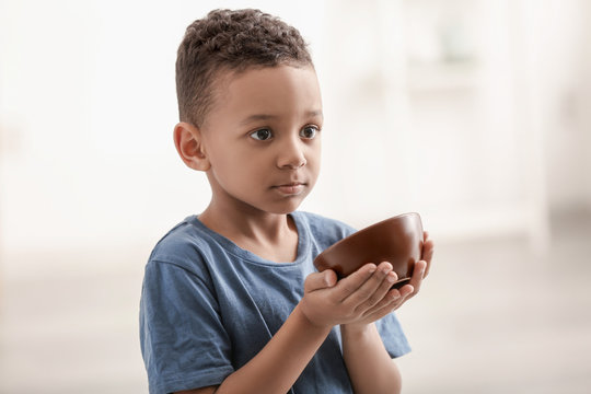 Cute little boy with bowl on blurred background. Poverty concept