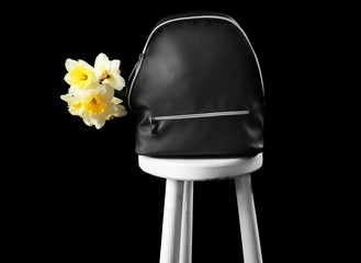 Leather backpack with flowers on stool against black background