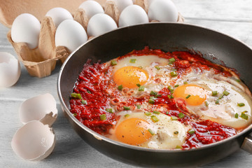 Frying pan with eggs in purgatory on wooden background