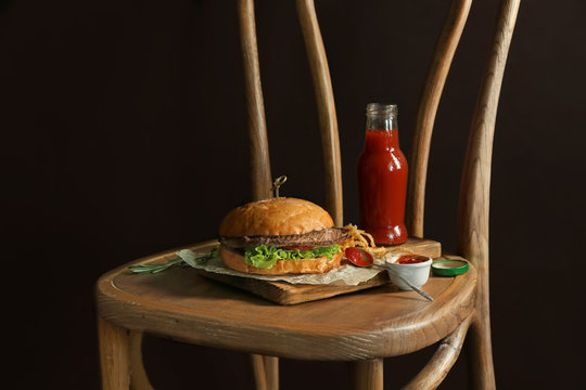 Composition with delicious burger with tomato juice on wooden chair