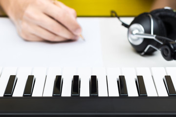 songwriter hands writing song with piano and headphone on desk, focus on piano keys