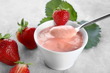 Composition of bowl and spoon with homemade strawberry yogurt on grey background