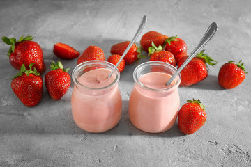 Composition with jars of fresh homemade yogurt and strawberries on grey background
