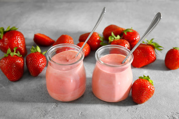 Composition with jars of fresh homemade yogurt and strawberries on grey background
