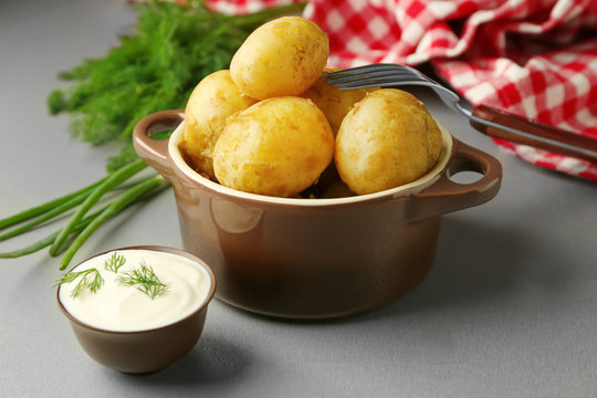 Pot with boiled potatoes, fresh herbs and sauce on table