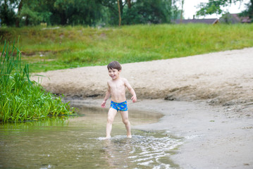 Happy little boy having fun and running in water in the river at summer day time, summertime lifestyle outdoor, friendly family weekend concept, healthy active lifestyle