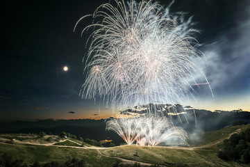 Fireworks on the top of the mountain in summer evening with moon in the sky