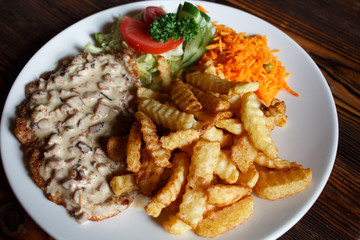 Traditional Latvian rustic dish: pork chop with cream sauce, carrot and cabbage salad, potatoes fries