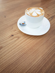 Cup cappuccino (with a flower pattern on the surface) on a wooden table with copy space