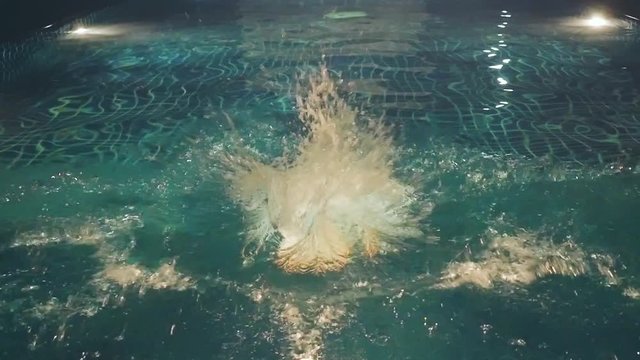 Young slim woman jumps and swims in a swimming pool at night time in slow motion. 1920x1080
