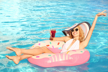 Beautiful young woman with glass of cocktail relaxing on inflatable donut in pool