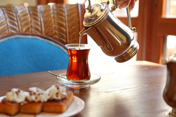 Pouring tasty Turkish tea into traditional glass in cafe