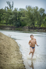 In the summer on the river the boy runs along the shore.