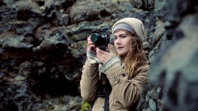 Young beautiful woman holding camera and taking photos in the mountains. Traveling female filming on the nature.